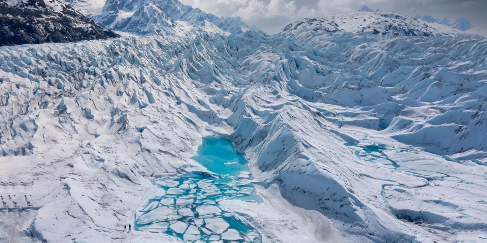 Aerial view of the crevassed glacier surface with meltwater pools breaking through the white ice