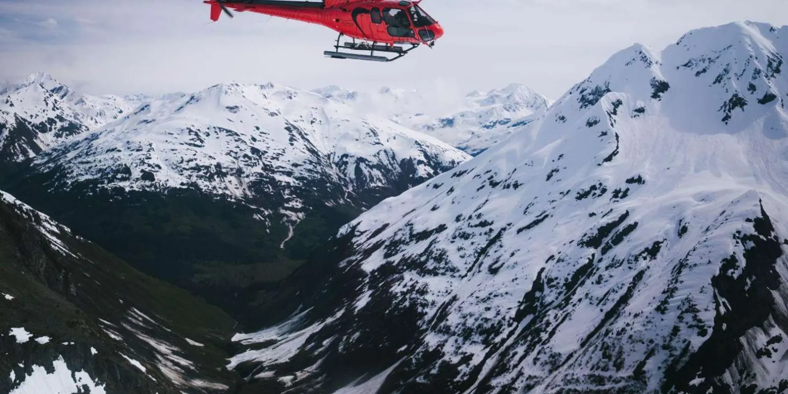 A red helicopter flying above the snow-covered Chugach Mountains on the way to Punchbowl Glacier
