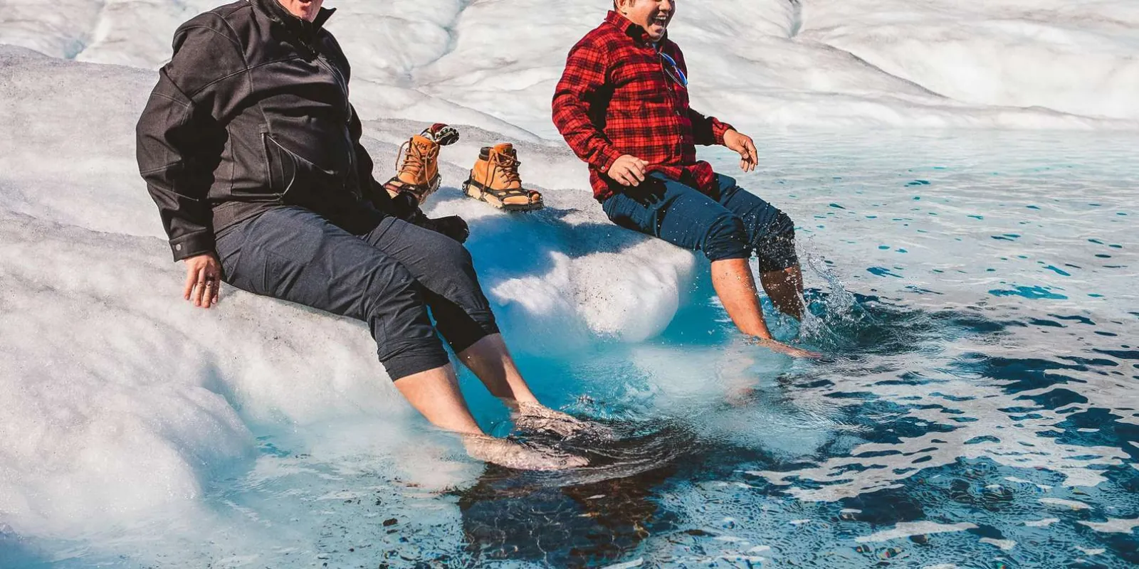 Two guests sitting on the glacier with their bare feet in the freezing turquoise meltwater