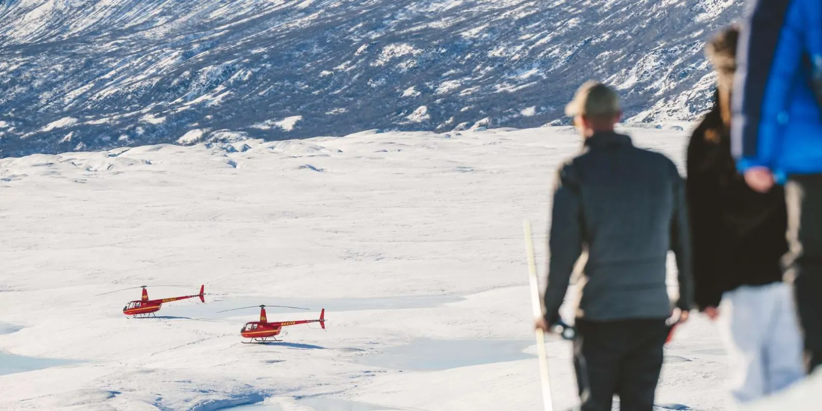 Guests walking on the snow with two small red helicopters parked further out on the glacier