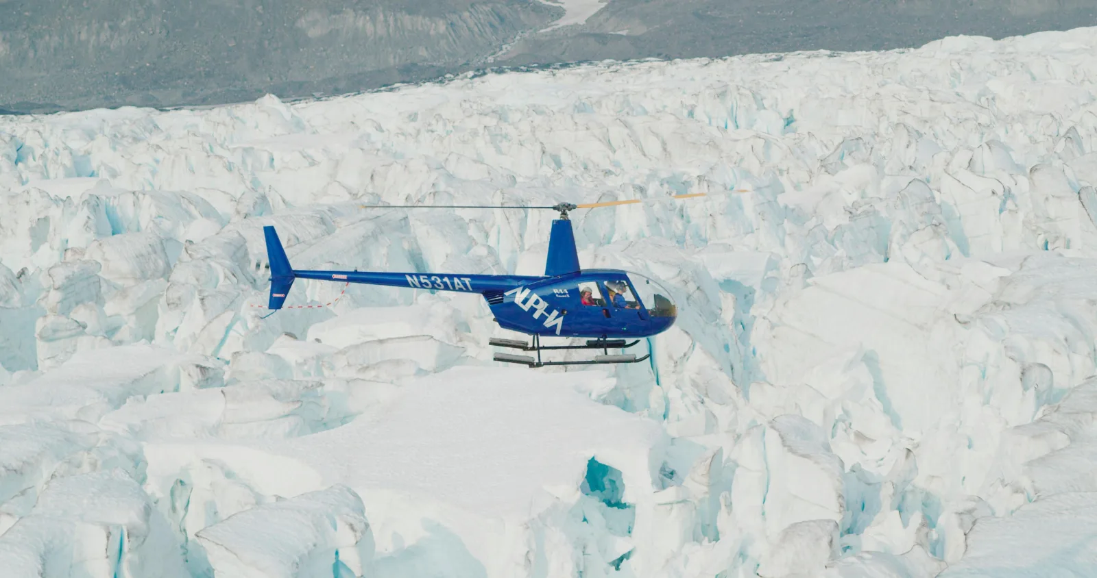 A blue helicopter flying low over the broken seracs of the glacier