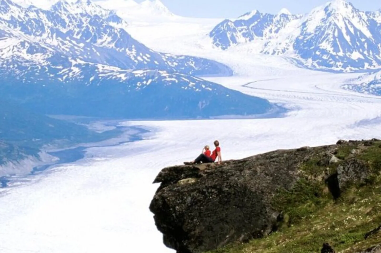 A guest sitting on a rock outcrop above the wide white sweep of the glacier