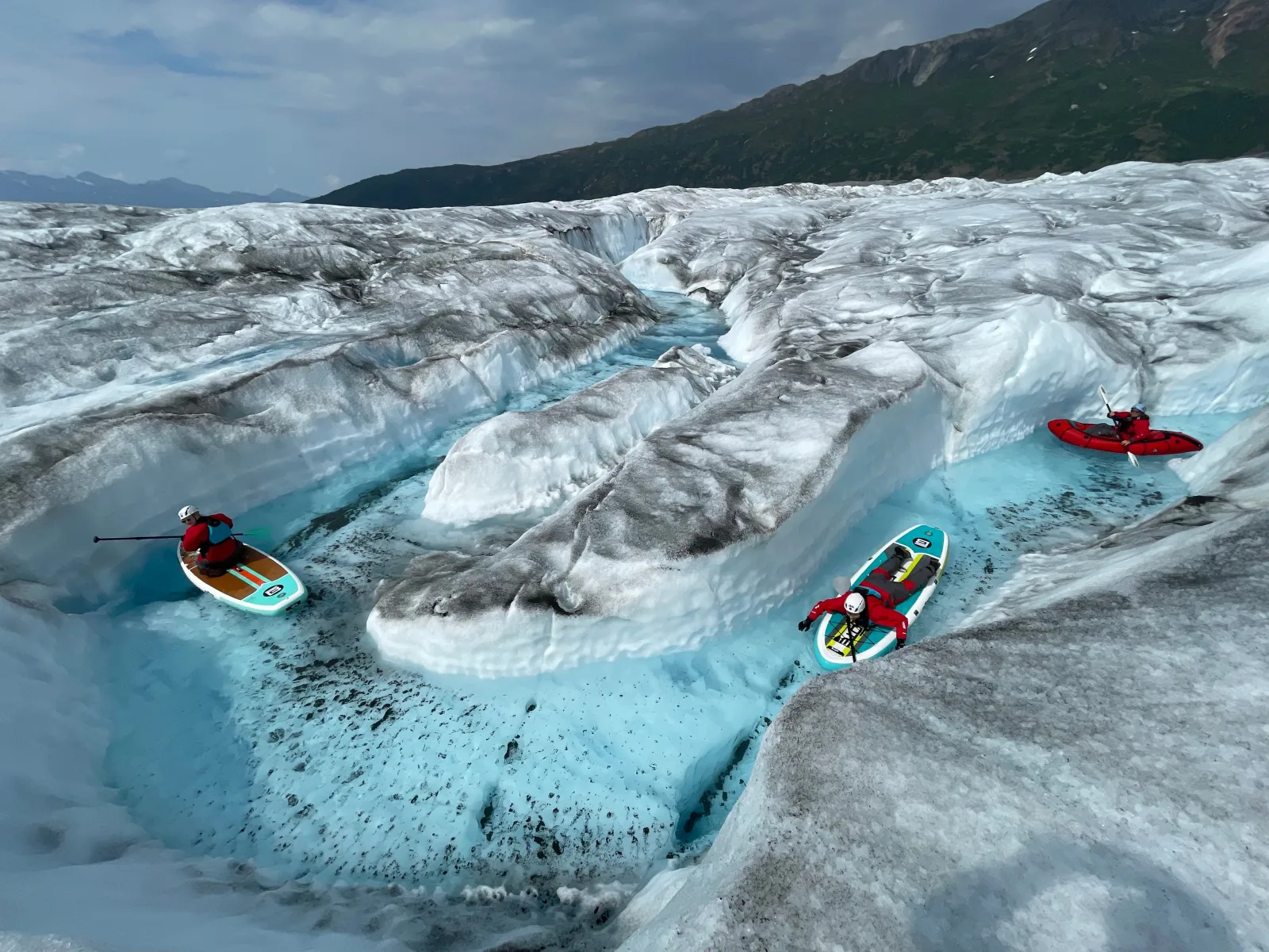 Paddleboards and a kayak drawn up on the ice beside a narrow glacial channel