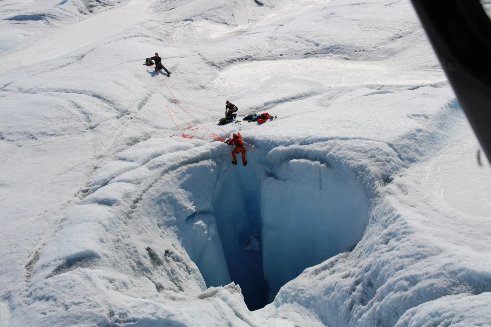 Aerial view of a small climbing party working around a deep blue moulin in the glacier surface