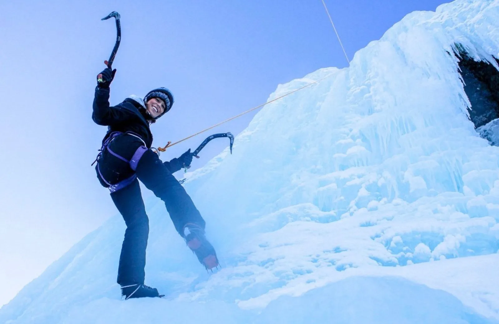 A climber swinging an ice axe into a near-vertical wall of glacier ice
