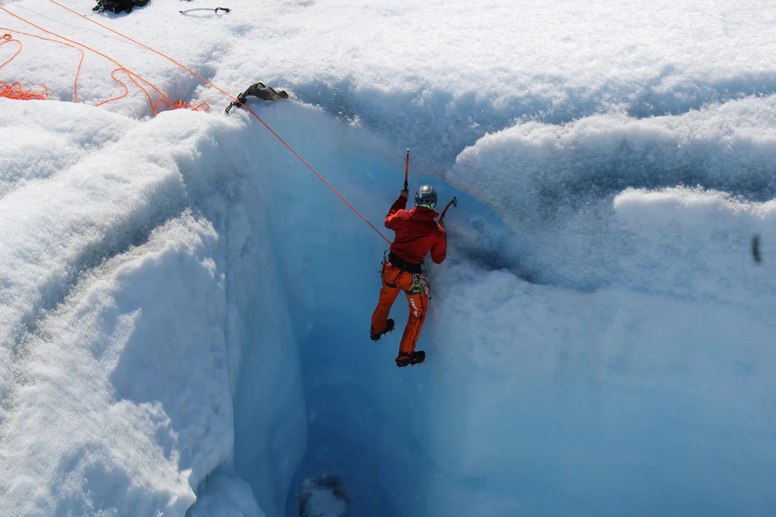 Two climbers on ropes descending into a crevasse on the glacier