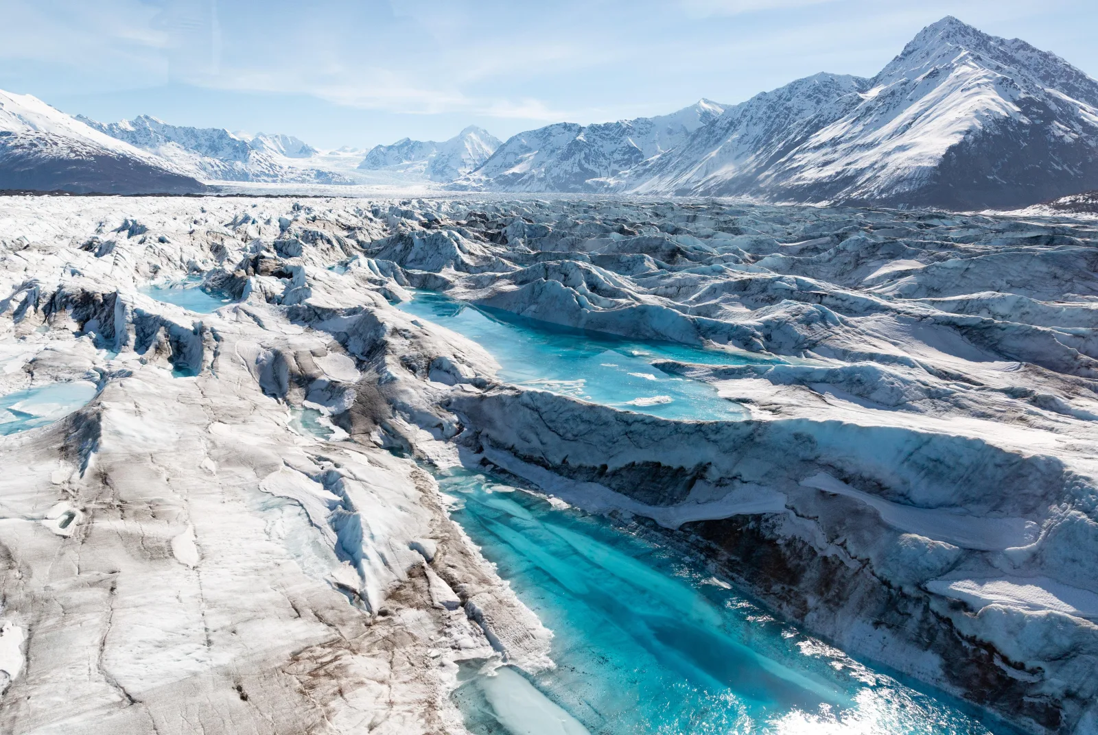 Aerial view along Knik Glacier, turquoise meltwater channels braiding through the blue ice